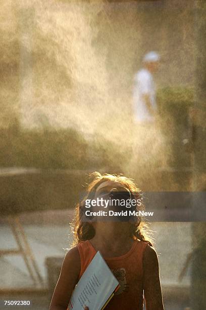 Girl tries to catch drops of cool water under a sidewalk cafe mister as temperatures hovers around 115 degrees Fahrenheit July 5, 2007 in Palm...