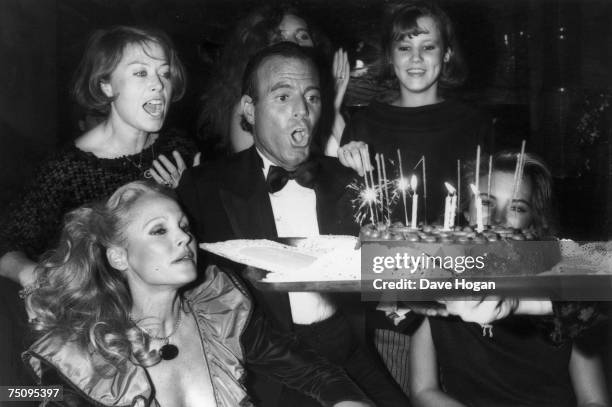 Spanish singer Julio Iglesias blows out the candles on his birthday cake, 1983. Swiss actress Ursula Andress is among the guests.