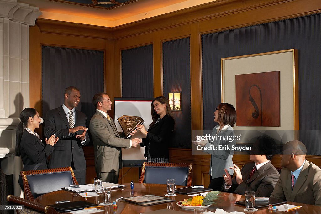 Business people in conference room, business man receiving award while colleagues applaud