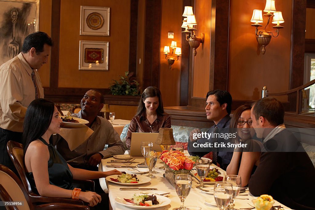 Group of people sitting at restaurant table, waiter serving meal