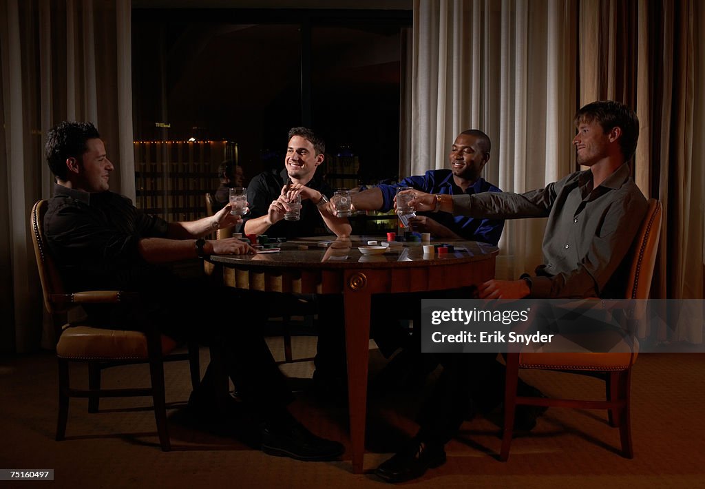Four men sitting at round table in dark hotel room, toasting