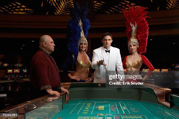 man throwing dices at roulette table, two dancers and senior casino worker next to him - casino interior photos et images de collection