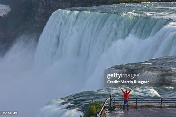 usa, new york state, niagara falls, man standing on lookout terrace with extended arms, elevated view - niagarawatervallen stockfoto's en -beelden