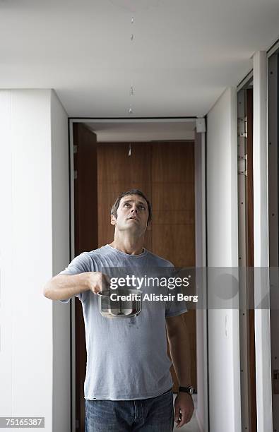 man standing in corridor, holding saucepan under leak in ceiling, looking up - leaking stock pictures, royalty-free photos & images