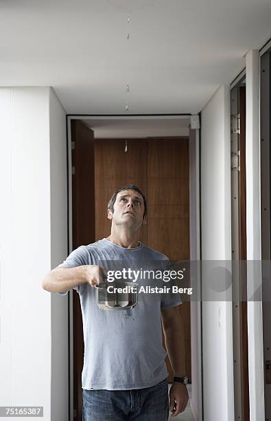 man standing in corridor, holding saucepan under leak in ceiling, looking up - leaking - fotografias e filmes do acervo