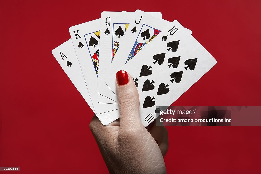 Woman's hand holding 'Royal Flush' hand of cards