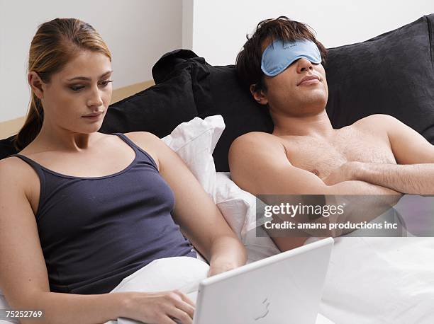 young woman using laptop on bed, boyfriend sleeping - computer wearing eye mask stock pictures, royalty-free photos & images