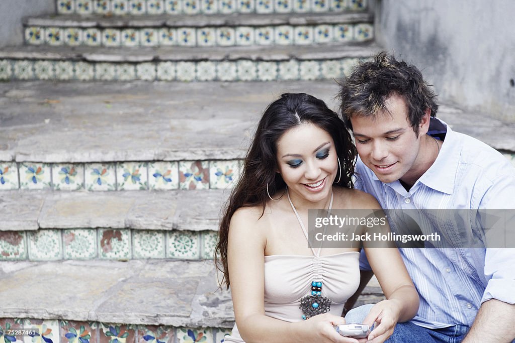 Young couple sitting on steps, woman using mobile phone