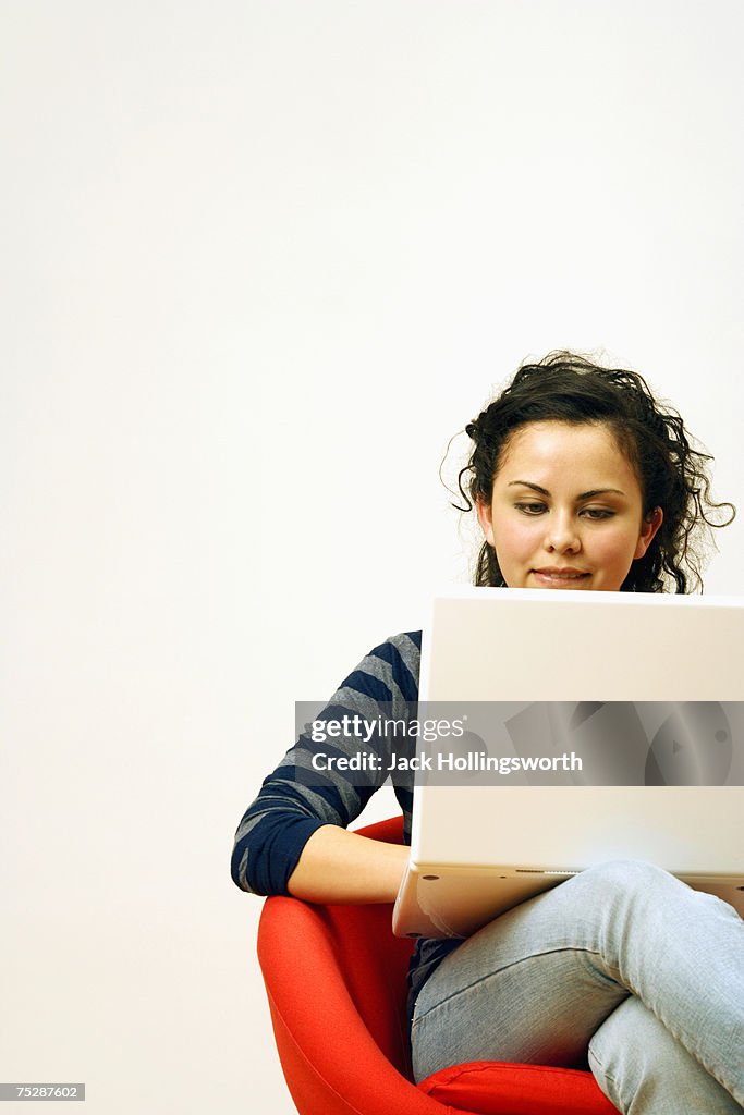 Girl (14-15) using laptop, sitting on chair, smiling