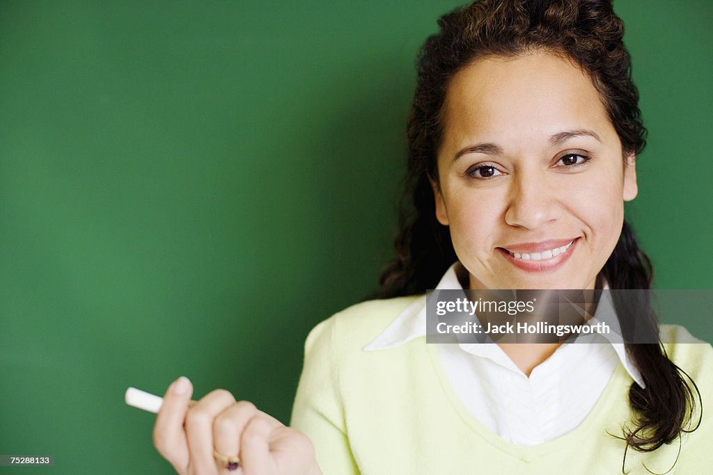 Teacher holding chalk in classroom, smiling, portrait