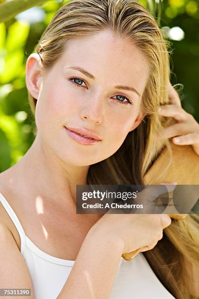 portrait of a young woman looking at the camera, brushing her hair, outdoors - brushing hair stock pictures, royalty-free photos & images