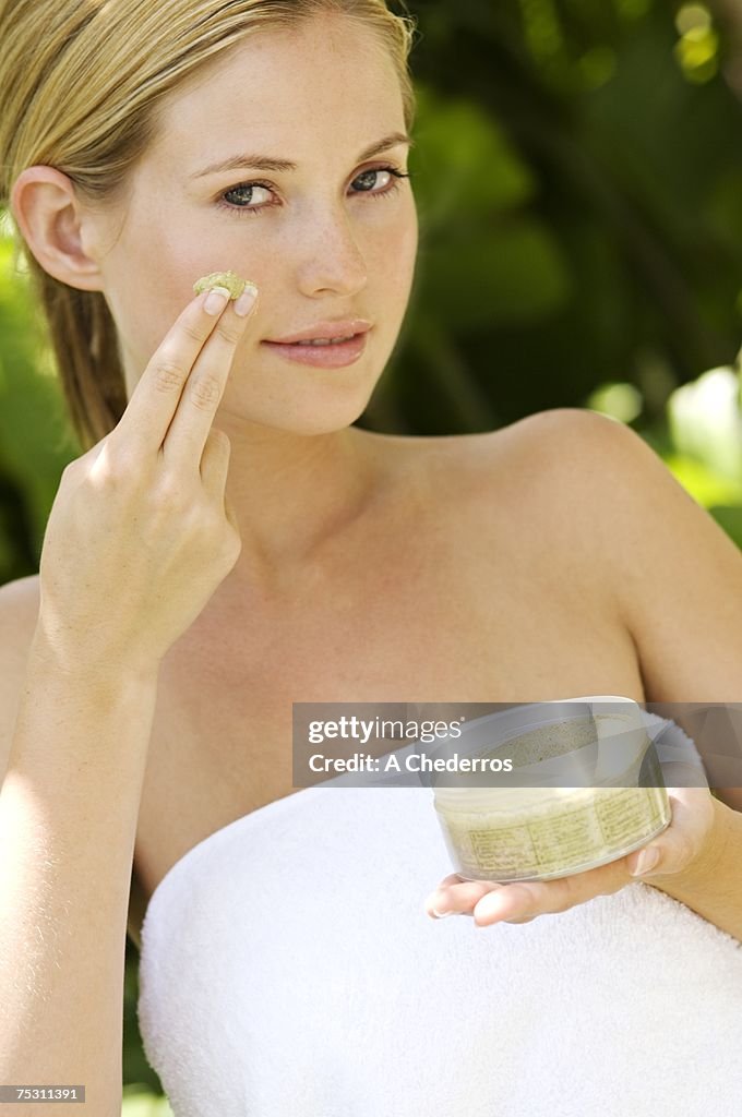 Young woman applying face scrub cream on her face, outdoors