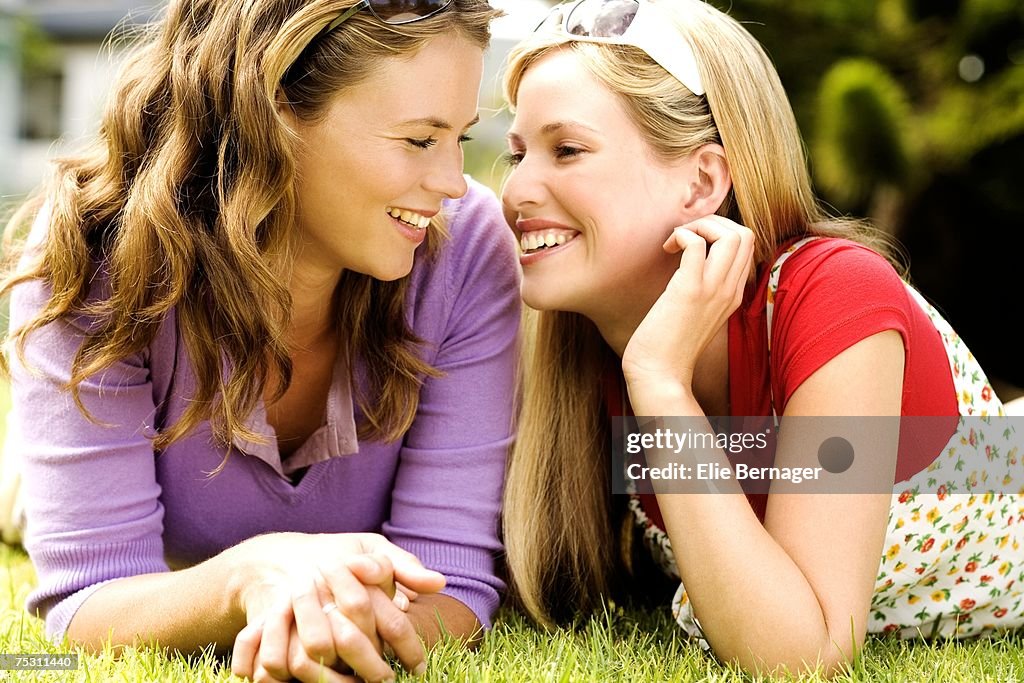 2 young smiling women lying on grass, looking at each other