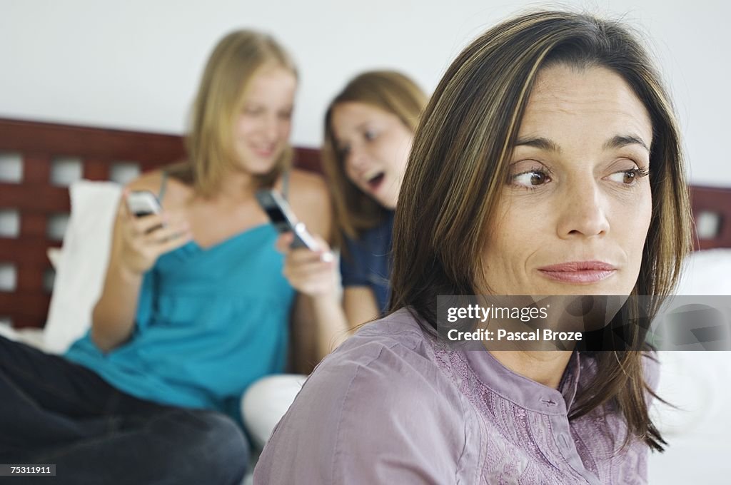 2 teenage girls sitting on bed, using mobile phones, thinking woman in foreground
