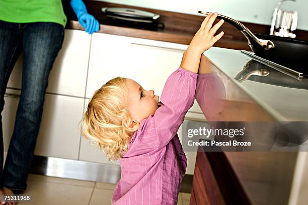 little girl in kitchen trying to catch a frying pan on stove, indoors - attraper photos et images de collection