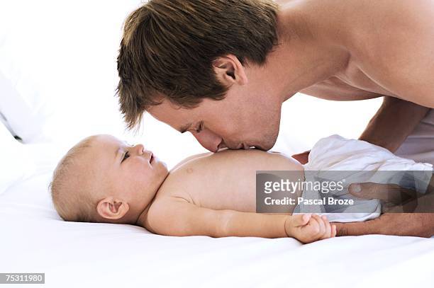 portrait of a father kissing his baby's chest, lying on bed, indoors - chest kissing 個照片及圖片檔