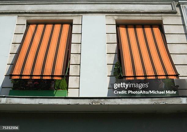 two striped awnings pulled down over windows, low angle view - striped awning stock pictures, royalty-free photos & images