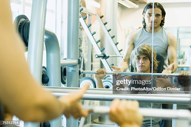 man lifting barbell while second man spots - rear view mirror stockfoto's en -beelden
