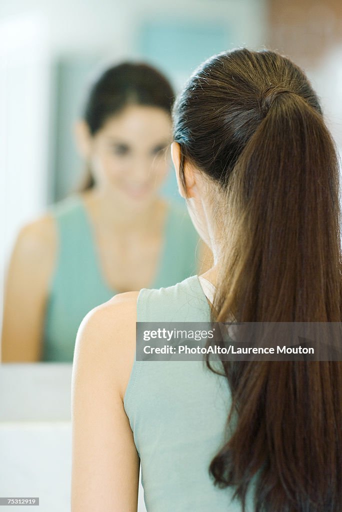 Woman looking at self in mirror, rear view