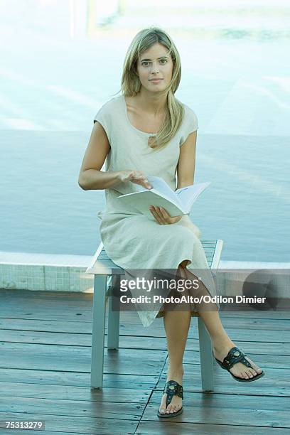 woman sitting and holding book, water in background - sfogliare libro foto e immagini stock