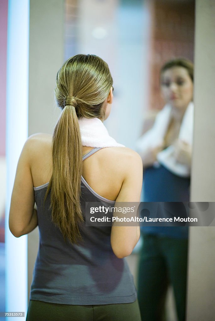 Young woman looking at self in mirror, rear view
