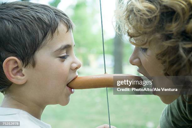 boy holding hotdog in mouth while second boy takes bite out of other end - chewing with mouth open stock pictures, royalty-free photos & images