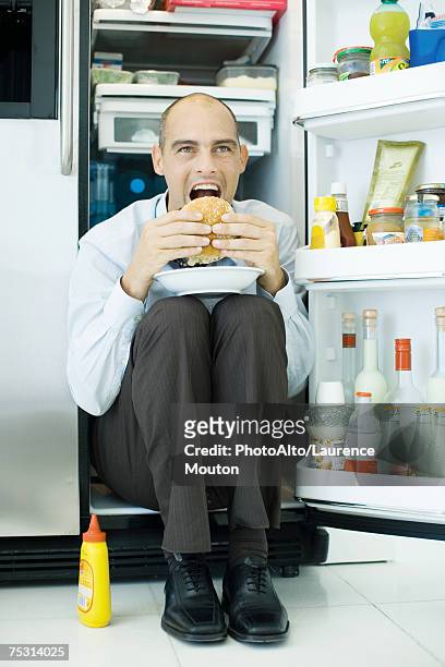 man sitting inside refrigerator, eating sandwich - funny fridge stock pictures, royalty-free photos & images