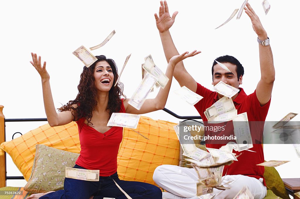 Young couple sitting on the bed and bank notes falling on them