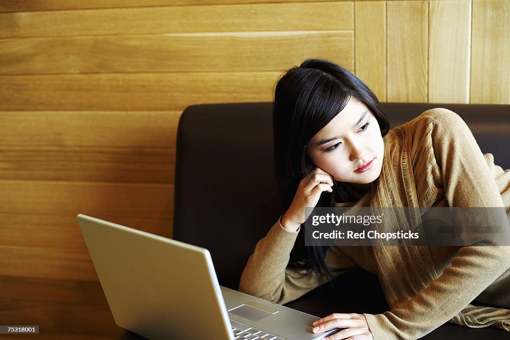 Close-up of a young woman lying on a couch in front of a laptop
