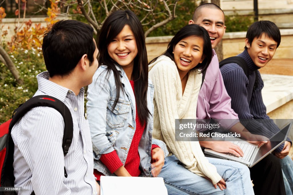 Five young college students sitting together in a college campus and smiling