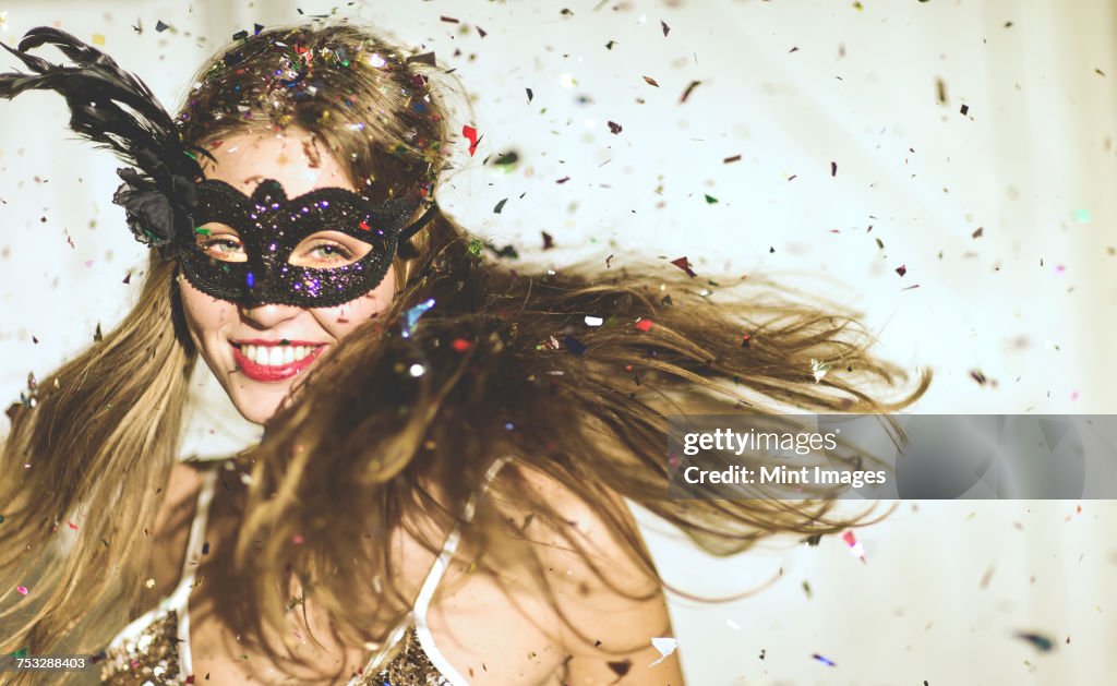 Young woman wearing a black eye mask at a party with confetti falling.