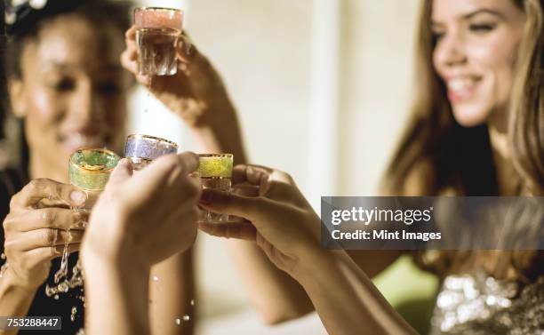 two young women at a party in sequined dresses drinking and laughing, one wearing a face mask.  - glamour shot stock pictures, royalty-free photos & images