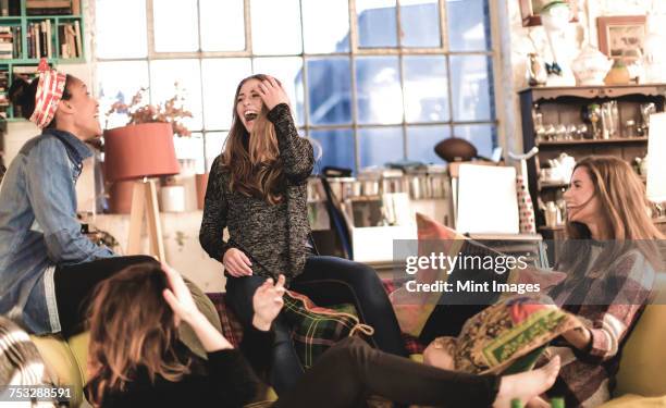 four young women sitting indoors on a sofa, laughing. - girls night in stock pictures, royalty-free photos & images