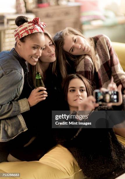 four young women sitting on a sofa, smiling, taking a selfie, holding beer bottles. - girls' night in stock pictures, royalty-free photos & images