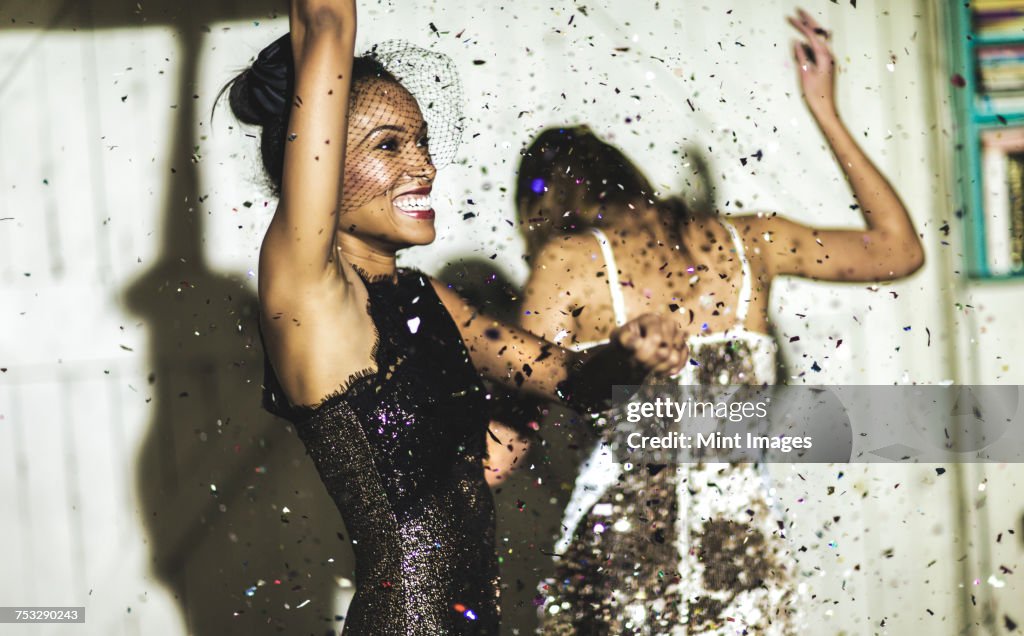 Two women wearing cocktail dresses at a party dancing in a shower of glitter confetti.