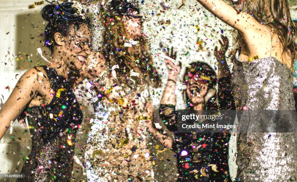 Four women wearing cocktail dresses dancing in a shower of confetti.