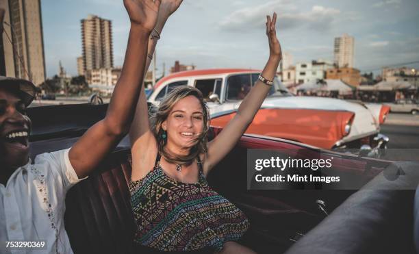 two people riding through a city in an open convertible with their arms raised. - v cuba stock-fotos und bilder