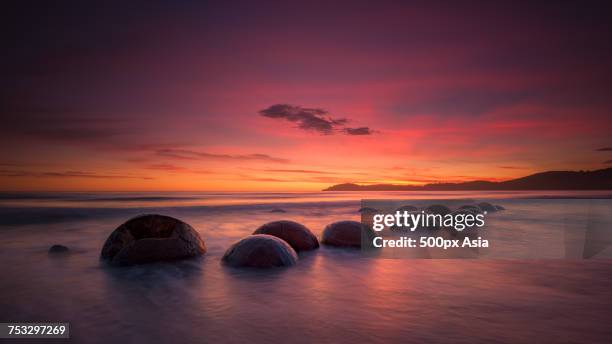 moeraki boulders on beach under romantic sky at sunset, koekohe beach, new zealand - moeraki boulders stockfoto's en -beelden