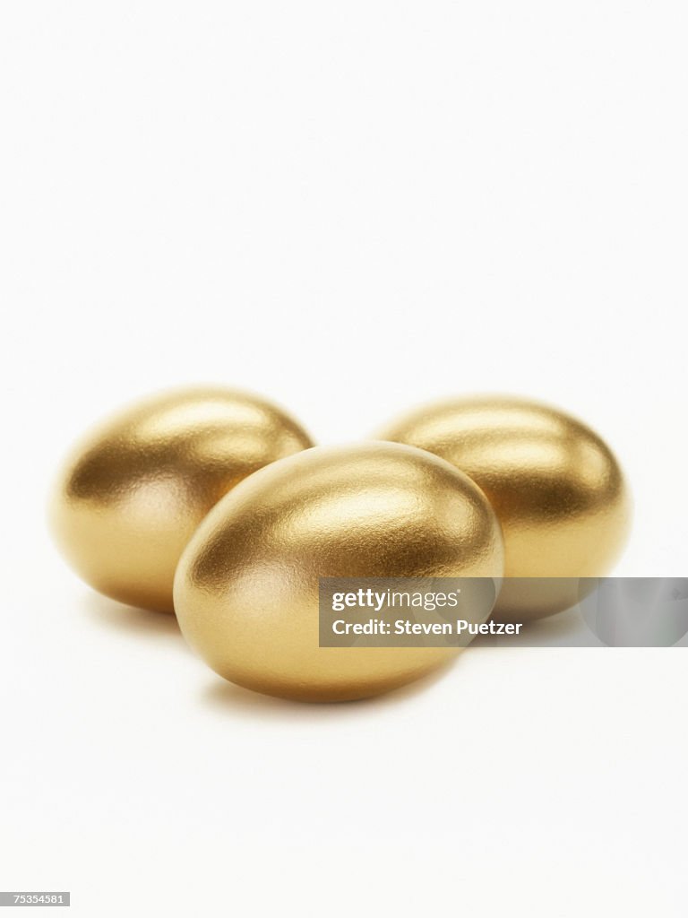 Three golden eggs against white background