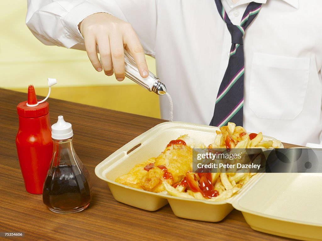 Boy (8-10) pouring salt on fish and chips