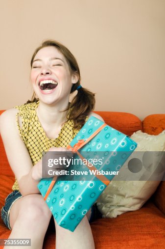 Teenage girl (16-18) sitting on sofa holding present, smiling Teenage girl (16-18) sitting on sofa holding present, smiling