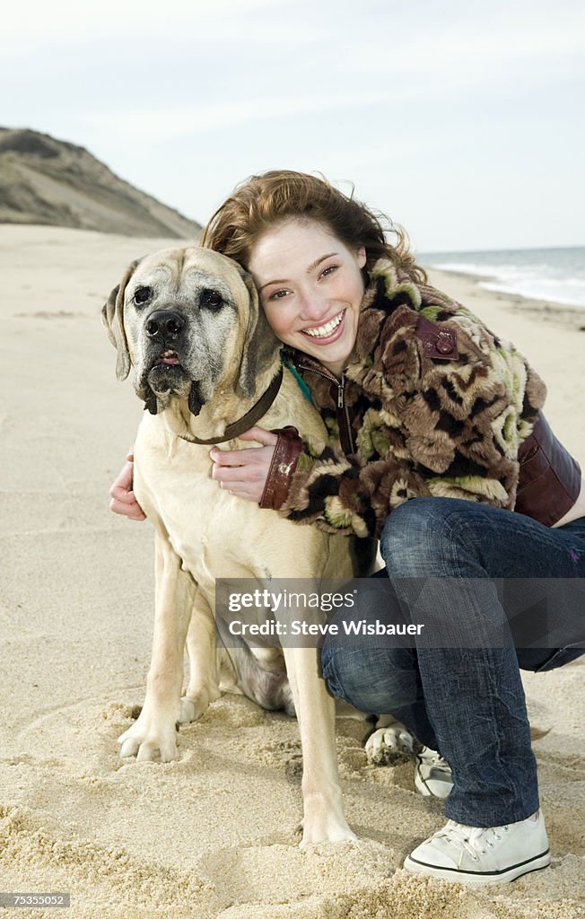 Teenage girl (16-18) crouching by dog on beach, smiling, portrait