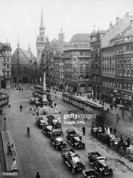 The Marienplatz in Munich, with the Altes Rathaus at the top left, with the tower, circa 1925. The Mariensaule, a golden statue of the Virgin Mary...