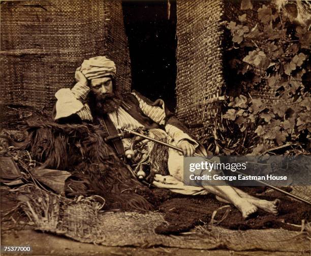 Entitiled 'Arab Reclining,' portrait of a man in traditional middle eastern clothing, including a turban, as he reclines, eyes closes, on a woven...