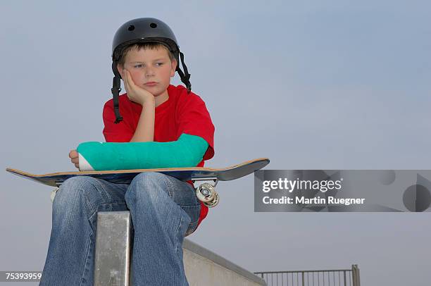 boy (8-9) sitting with skateboard, arm in plaster - broken skateboard stockfoto's en -beelden