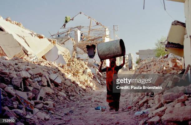 Woman carries a vessel to her tent through the rubble of Kadila, a village on the outskirts of Bhuj, India February 6, 2001 following an earthquake...