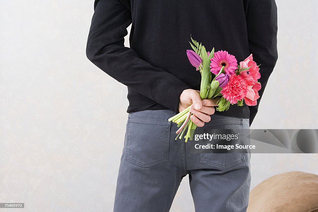 Mann hält Blumen hinter dem Rücken