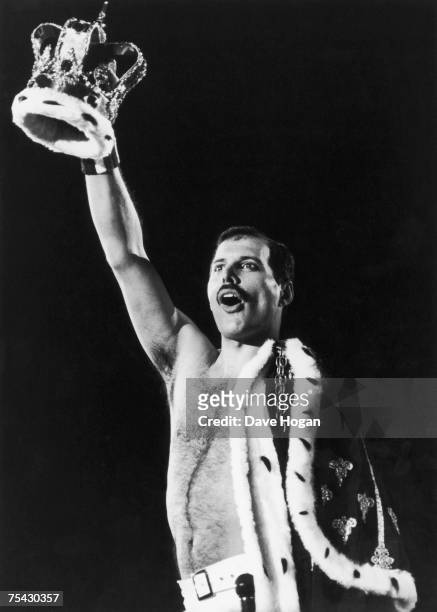 Regally attired Freddie Mercury , of British rock group Queen, raises a crown during a performance, 1986.