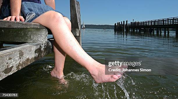 Young woman cools her feet while sitting on a boardwalk at the Ammersee Lake on July 16, 2007 in Diessen am Ammersee, Germany. The heatwave is...