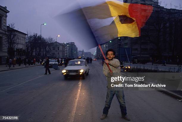 An anti-Ceausescu protestor waves a torn Romanian flag during the Romanian Revolution, December 1989. The Communist coat of arms has been removed...